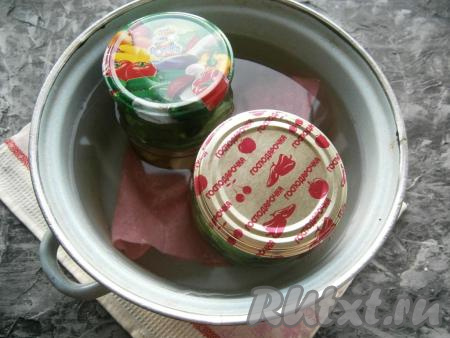 Поставить банки с заготовкой в кастрюлю с тёплой водой, на дно которой поместить тряпочку (если тряпочка тонкая, сложите её в 2-3 раза). Довести воду до кипения на среднем огне и затем стерилизовать банки с огурчиками 15 минут.