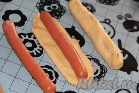 Готовое тесто разделить на 8-10 частей. Раскатать каждую часть теста в овал по длине сосиски. Сосиску выложить на тесто и, завернув её в тесто, хорошо защипать шов.