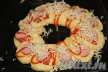 Сыр предварительно нетереть на мелкой тёрке. Посыпать сосиски в тесте сыром.