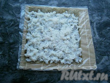 Лист нори выложить на циновку так, чтобы сверху была шершавая сторона листа. Разместить и разровнять по всему листу приготовленный рис, не доходя около 1 см до верхнего края нори.