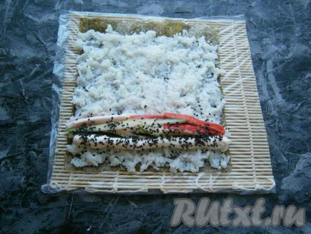 Рядом с огурцом нанести 1-2 полосы сливочного сыра (лучше сыр поместить в кулинарный мешок, обрезав его кончик) и посыпать сверху кунжутом.