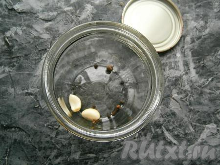 На дно простерилизованной сухой банки поместить 2 зубчика чеснока, горошины чёрного перца, гвоздику, горошины душистого перца.