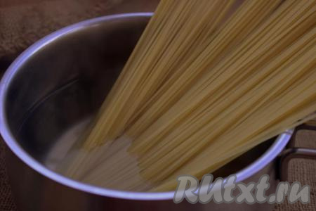 Тем временем отварить спагетти, для этого в широкую кастрюлю влить воду, поставить на огонь. Когда вода закипит, посолить её, уменьшить огонь, выложить спагетти, аккуратно перемешать и варить до готовности (продолжительность варки можно посмотреть в инструкции на упаковке). Готовые спагетти откинуть на дуршлаг, дать стечь воде.