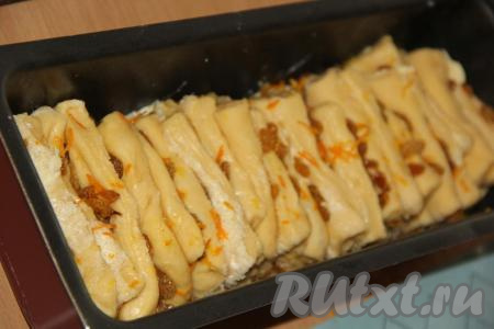 Тесто разрезать на 6 продольных полосок. Каждую полоску разрезать на 5 частей. Из каждой полоски получится 5 прямоугольников. Обдать изюм кипятком и откинуть на дуршлаг. Затем вымыть апельсины и снять с них цедру. Соединить изюм с цедрой и перемешать. Выложить изюм с цедрой на каждый прямоугольник теста и свернуть его пополам, как бы заворачивая внутрь начинку.&nbsp;Форму для выпечки (я использовала прямоугольную форму для кекса) смазать растительным маслом. Прямоугольники с начинкой, сложенные пополам, выложить в форму сгибом вниз (как на фото) и оставить на 1 час в тепле для расстойки.