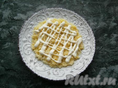 Картошку предварительно отварить в кожуре до готовности (варить минут 20-25), затем остудить. Куриные яйца отварить в течение минут 10 с момента закипания воды, дать им остыть. Очистить варёный картофель и натереть его на средней тёрке. Выложить натёртую картошку на плоскую тарелку первым слоем, посолить, смазать майонезом.