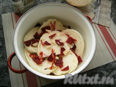 В кастрюлю складывать ломти капусты рядами, пересыпая их свеклой, чесноком и колечками горького перца.