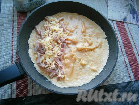 В сковороде разогреть сливочное и растительное масло, затем вылить омлетную смесь. Прикрыть крышкой и жарить на небольшом огне до тех пор, пока верх омлета не станет почти сухим. Далее на одну сторону омлета выложить ветчину и сыр (немного сыра оставить для подачи).