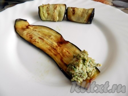 На ломтик баклажана выложить часть орехово-чесночной массы и скрутить в рулетик, начиная со стороны с начинкой.