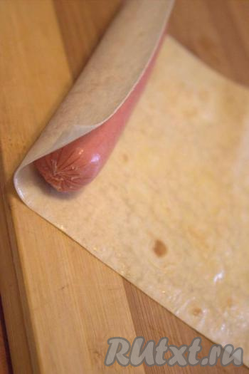 На край полоски из лаваша выложить сосиску и свернуть лаваш в плотный рулет. Аналогично сформировать и все остальные рулеты из лаваша с сосиской внутри.