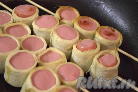 Разогреть растительное масло в сковороде, выложить сосиски в лаваше на шпажках и обжарить на среднем огне с двух сторон до золотистого цвета (примерно, по 3 минуты с каждой стороны).