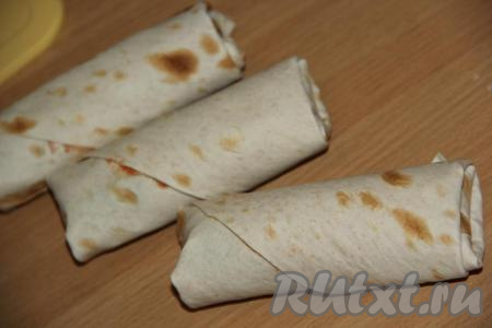 Края каждого квадрата из лаваша подвернуть с двух сторон, а потом свернуть рулетом. Получатся рулетики&nbsp;из лаваша с начинкой из сосисок, сыра и огурцов.