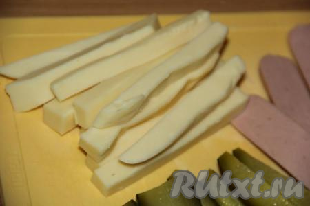 Сыр нарезать на брусочки такой же длины, как нарезаны сосиски и огурцы.