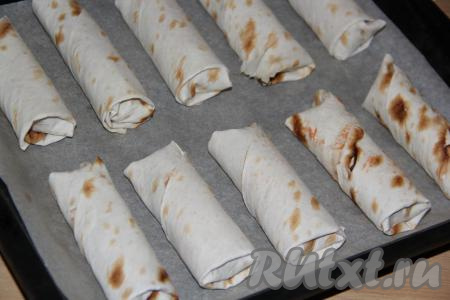 Противень застелить пергаментом. Рулетики из лаваша с начинкой из&nbsp;сосисок,&nbsp;сыра и огурчиков поместить на противень и поставить в разогретую духовку.
