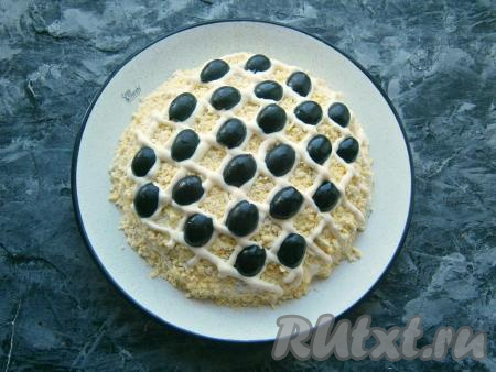 В ячейки сетки из майонеза, через одну, разместить половинки чёрных оливок, имитируя семечки. Оливки нужно выкладывать в ячейки из майонеза в шахматном порядке (как на фото).