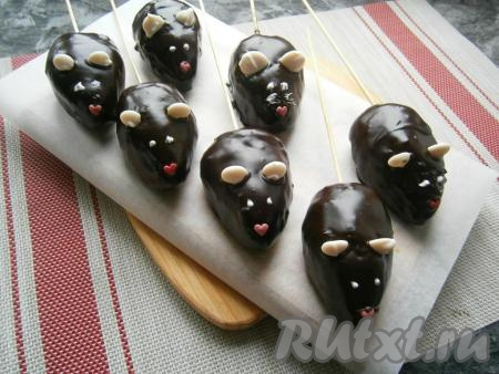 Подготовленных "мышек", держа за шпажку, окунуть в чуть остывшую глазурь, поместить на досочку, застеленную пергаментом. Сразу же&nbsp;вставить ушки из капель белого шоколада, сделать глазки в виде точек из растопленного белого шоколада и носики из кондитерской посыпки.