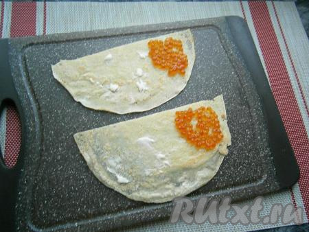 Смазать половинки тёплых блинов размягчённым сливочным маслом (для того чтобы масло размягчилось, заранее достаньте его из холодильника) и на одну сторону блина выложить по 1-2 чайных ложки&nbsp;красной икры.