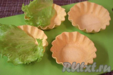 Для того чтобы тарталетки не размякли, не потеряли форму и оставались хрустящими, наполнять салатом их нужно непосредственно перед подачей закуски на стол. В каждую тарталетку выложить листик зелёного салата.