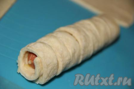 Выложить сосиску перпендикулярно надрезам и закрутить в тугой рулетик. Также сформировать оставшиеся три заготовки. Затем из второго пласта слоёного теста тоже сделать 4 квадрата с надрезами, выложить сыр и сосиски, свернуть в плотные рулетики. В результате из двух пластов теста получится 8 заготовок.