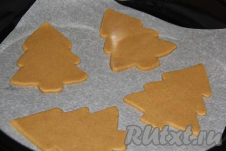 Охлаждённое тесто разделить на 4-6 частей. Пока вы будете работать с одной частью теста, оставшееся тесто пусть будет в холодильнике. Одну часть теста скалкой раскатать в пласт толщиной 5-7 мм. Вырезать пряники в виде ёлочек (для того чтобы вырезать ёлочки, можно взять готовые покупные формочки, а можно вырезать трафарет из бумаги, приложить его к раскатанному тесту и ножом вырезать из теста ёлки). Выложить заготовки в виде ёлочек на противень, застеленный бумагой для выпечки.