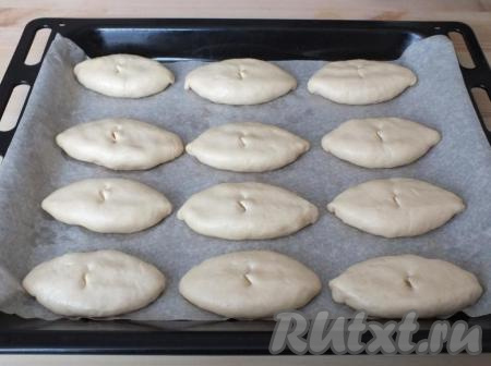 На противень, застеленный бумагой (или смазанный маслом), переложите пирожки швом вниз. Сверху на каждом пирожке, при помощи ножниц, сделайте надрезы - они необходимы для выхода пара.&nbsp;Духовку разогрейте до 180 градусов.