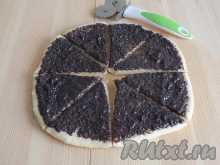 Возьмите одну часть теста. На столе, припылённом мукой, раскатайте тесто в круг толщиной 0,5 см. Смажьте поверхность теста половиной маковой начинки. С помощью резака (или ножа), разделите круг на 8 треугольников.