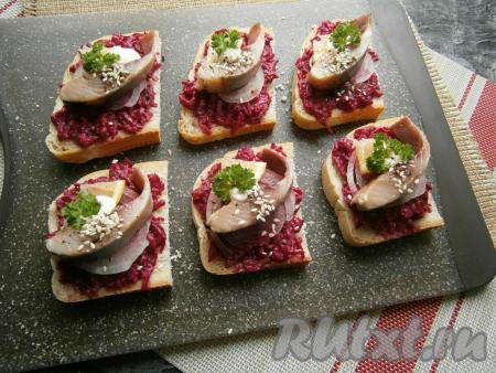 На каждый бутерброд со свеклой и луком выложить по кусочку селёдки, по маленькому кусочку лимона, посыпать сверху немного чёрным молотым перцем и кунжутом, украсить зеленью петрушки.