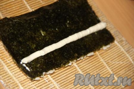 Перевернуть лист рисом вниз. Творожный сыр, поместив в кулинарный мешок, отсадить ровной полоской на нори, отступив пару сантиметров от края листа. Сыр нужно размещать с противоположной стороны от края, на обратной стороне которого нет риса.
