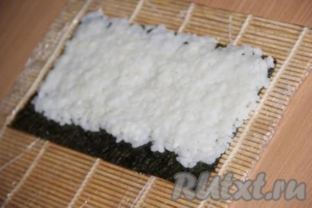 На циновку выложить половинку листа нори блестящей стороной вниз. Смоченными в воде руками выложить рис на лист нори, равномерно распределить, оставляя, один край нори (примерно, 1 см) свободным (как на фото).