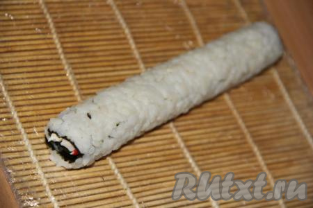 С помощью циновки свернуть нори с начинкой в плотный ролл так, чтобы рис оказался снаружи. Начинаем заворачивать со стороны, где край с рисом, а пустой край листа нори закрепляет ролл.