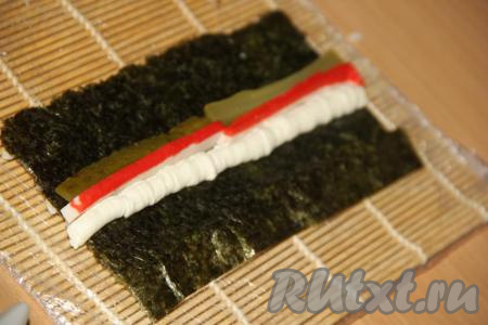 Брусочки маринованного (или свежего) огурца выложить рядом с крабовой палочкой.