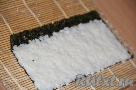 Лист нори разрезать на две половины. Выложить половину листа нори на циновку блестящей стороной вниз. Затем на нори выложить рис (толщина слоя риса должна быть около 5 мм). Равномерно распределить рис по листу, оставив от края 1 см листа нори, свободным от риса.