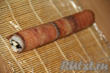 Рыбку прижать к рису с помощью циновки.