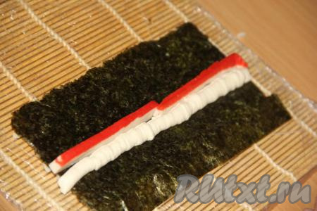 Каждую размороженную крабовую палочку разрезать вдоль на 2 или 3 части. Рядом с сыром выложить разрезанную крабовую палочку.