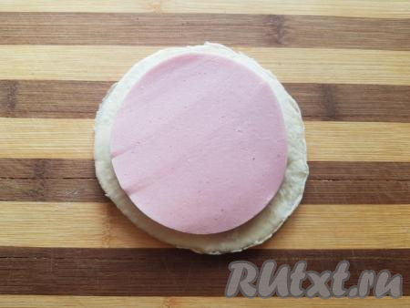 Сверху накрыть кружочком теста и выложить второй кусочек колбасы.