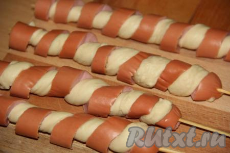 Жгутик теста обернуть по спирали вокруг шпажки (тесто нужно обматывать по надрезам на сосиске, как на фото). Таким образом сформировать все сосиски в тесте на шпажках.