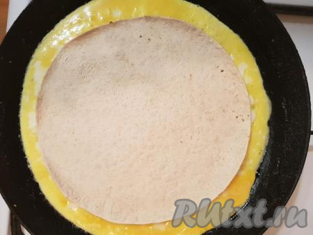 Когда яичница хорошо "схватится" (на её поверхности не будет жидких участков), выложите по середине лист лаваша круглой формы (у меня диаметр лаваша 20 см). Я использовала круглый лаваш, если у вас лаваш другой формы, то придайте ему нужную форму, приложив к нему тарелку нужного диаметра и обрезав по краю тарелки.