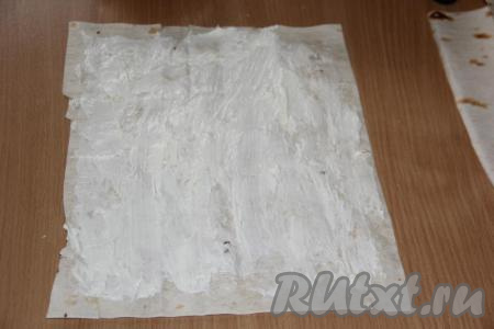 Одну часть лаваша, оставляя края лаваша чистыми, смазать половиной смеси из творожного сыра и чеснока.