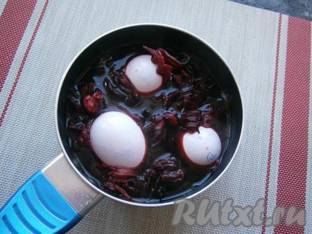 Когда чай с водой закипит, влить 1 столовую ложку уксуса, перемешать и выложить яйца. Яйца должны быть полностью покрыты и водой, и лепестками каркаде.