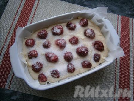 Форму размером 22х15 см застелить пергаментом и выложить в неё тесто, разровнять. Сверху разложить ягоды клубники, не размораживая их, посыпать 20 граммами сахара.