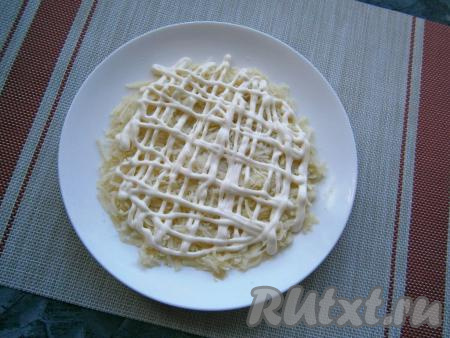 На плоскую тарелку выложить слой натёртого на средней терке картофеля, посолить и нанести сеточку из майонеза.