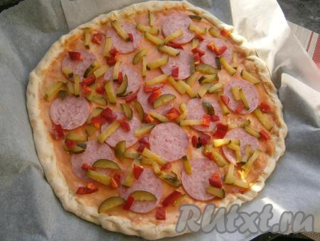 На тесто выложить колбасу, нарезанную на тонкие кружочки, а также солёный огурец, нарезанный брусочками, и нарезанный кубиками сладкий болгарский перец.