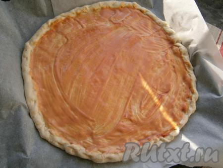 Далее тесто раскатать в большую лепёшку толщиной около 0,5 см (можно разделить тесто на 2 пиццы). Выложить лепёшку на противень, застеленный бумагой. Сделать небольшой бортик по краю теста. Смазать лепёшку кетчупом, смешанным с майонезом.