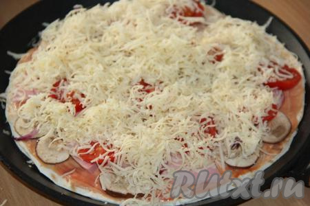 Поверх пиццы разложить кружочки помидоров, посыпать оставшимся натёртым сыром.