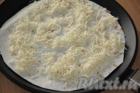 Сыр натереть на тёрке. Выложить один лист лаваша в сковороду (перед выкладыванием лаваша сковороду, при желании, можно немного смазать маслом), посыпать половиной натёртого сыра.