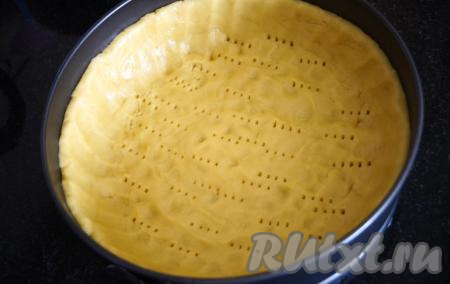 По прошествии времени достаём тесто из холодильника и равномерно распределяем по дну формы для выпечки (у меня форма диаметром 24 см), застеленной пергаментной бумагой, не забывая сформировать из теста бортики. Дно нашего пирога, для того чтобы оно не вздулось, прокалываем вилочкой.