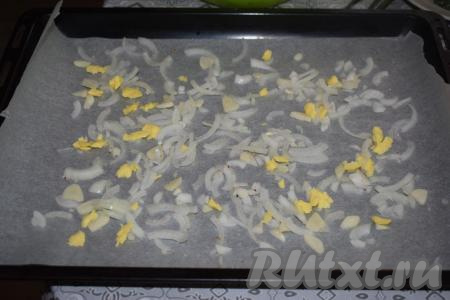 Подготовим противень, в котором планируем запекать наше блюдо. Застилаем дно противня пергаментом (фольга в данном случае не подойдёт, так как в рецепте используется молоко, а оно может пригореть на металлическом листе). Выкладываем на пергамент нарезанные лук и чеснок, раскладываем половину сливочного масла.