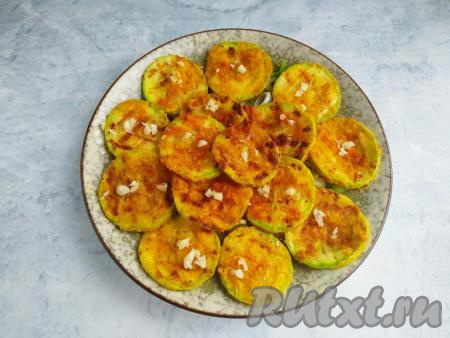 Сверху выложить кабачки, приготовленные в панировке на сковороде, посыпать их измельчённым чесноком.