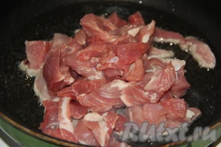 В сковороду влить немного растительного масла, разогреть. Выложить в разогретое масло кусочки свинины.