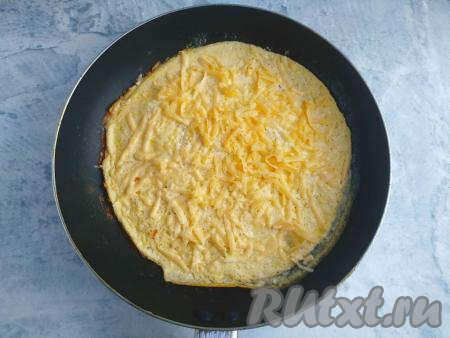 Сыр натереть на крупной тёрке, посыпать им омлет. Продолжить готовить блюдо под крышкой на минимальном огне около 1-2 минут (до расплавления сыра).