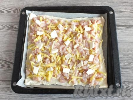 Переложите один раскатанный пласт на противень, застеленный пергаментом. Сделайте на тесте в нескольких местах проколы вилкой. Выложите начинку, оставляя пару сантиметров по краям свободными.&nbsp;Распределите кусочки холодного сливочного масла поверх начинки.